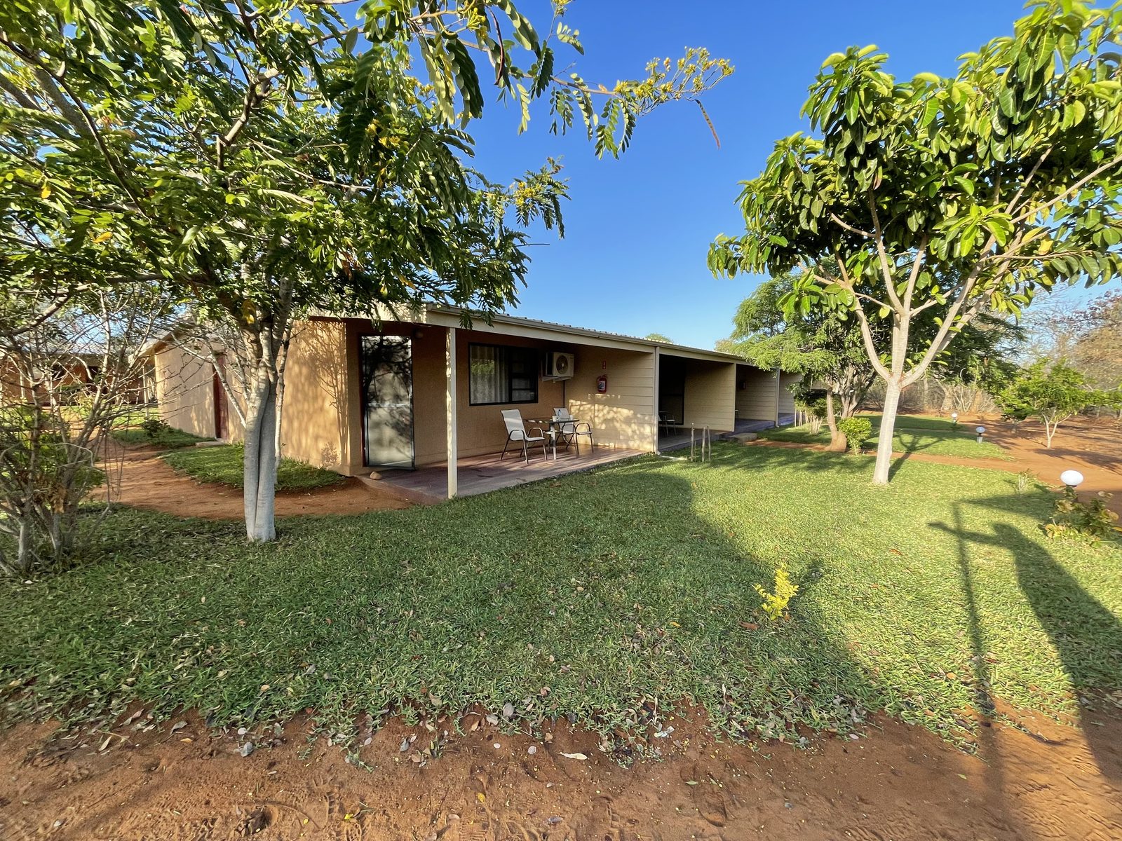 Chalets under mango trees on green lawn at the camp, deep blue sky, open country beyond