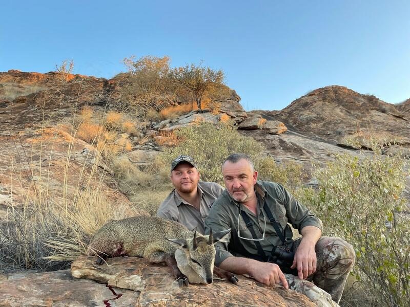 Two hunters seated on a rock outcrop